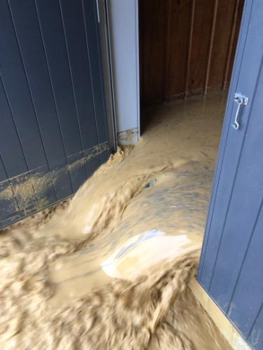 Muddy flood-waters pouring out of the Ōakura community hall. credit: Supplied / Glenn Ferguson