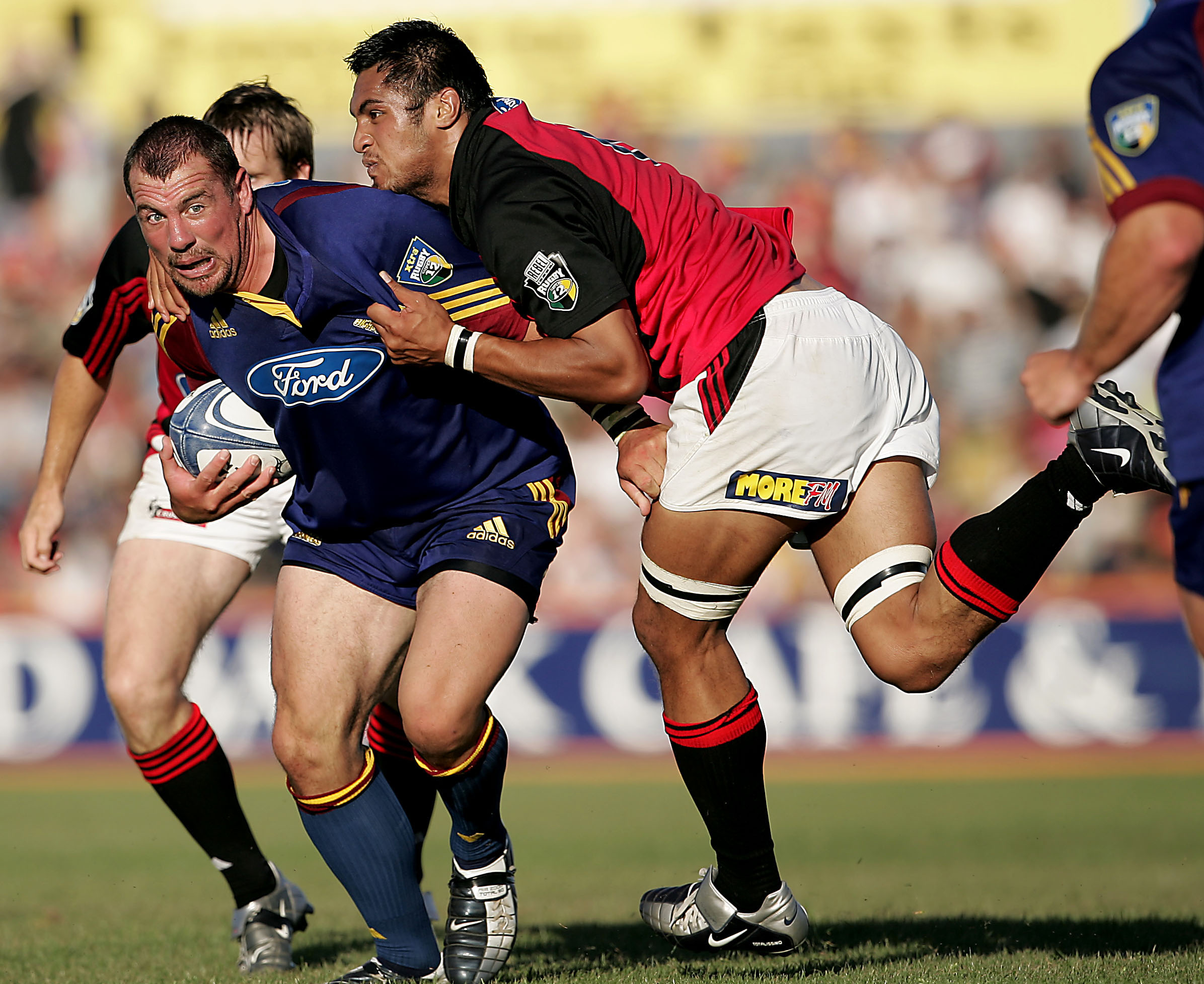 Otago Highlander Paul Miller looks to offload while in the tackle of Crusaders lock George Naoupu...