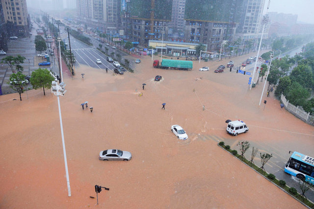 Pedestrians and vehicles cross a flooded street during heavy rain in Changsha, Hunan province,...