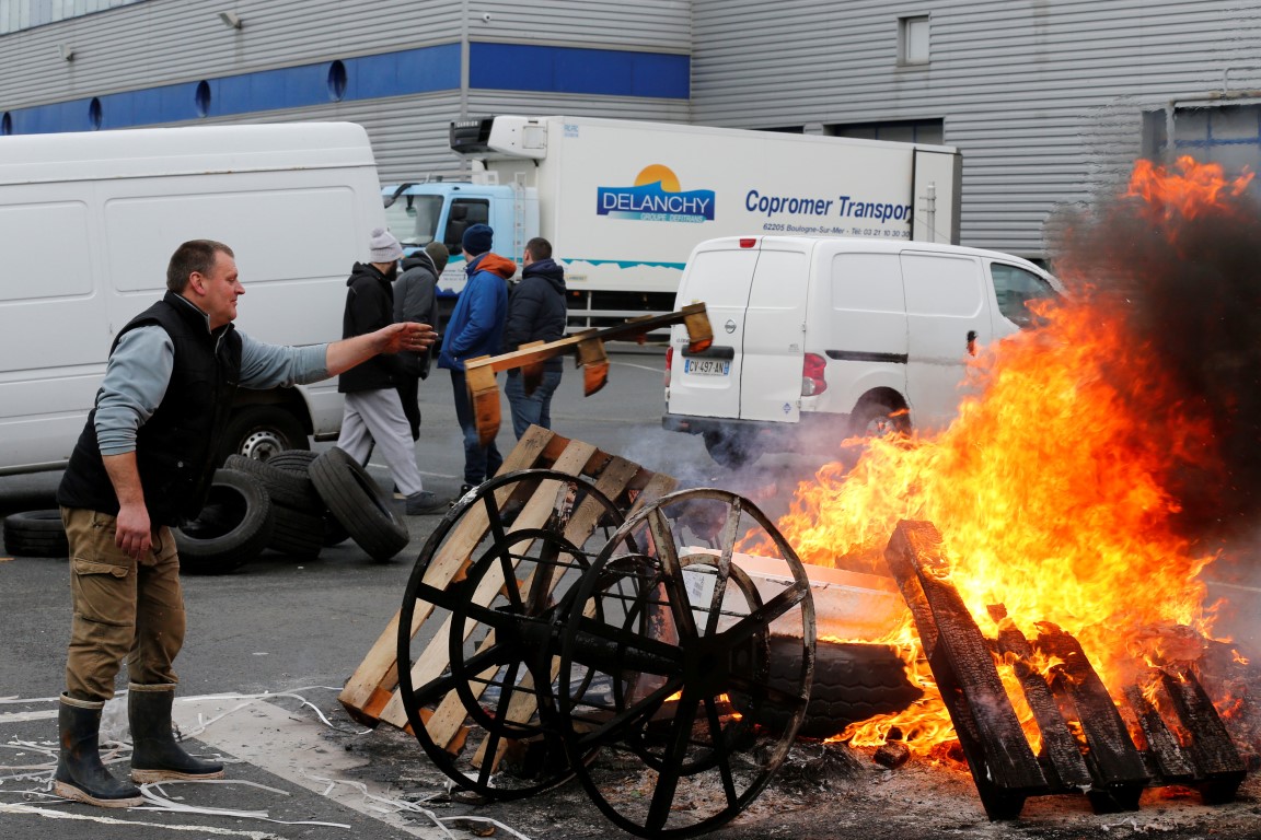 A fisherman puts a tyre on to a fire at a road block during a protest against electric pulse...