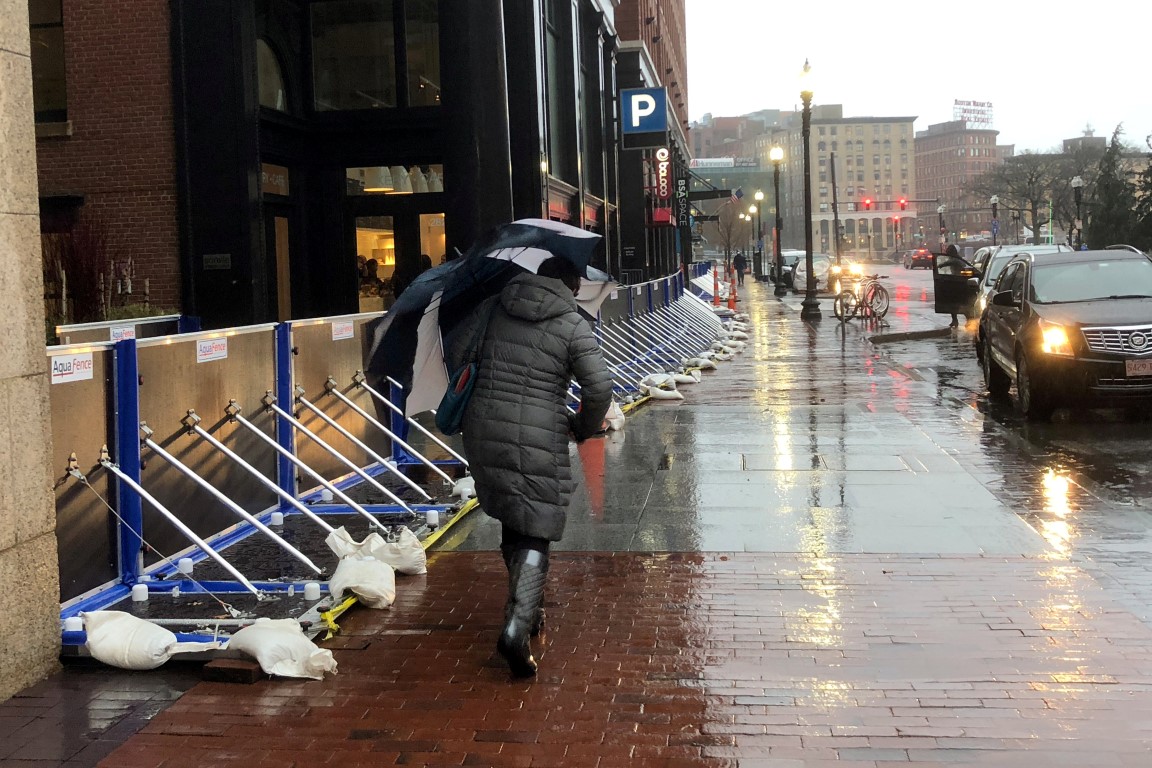 People walk past an office building protected by temporary flood barriers in Boston,...
