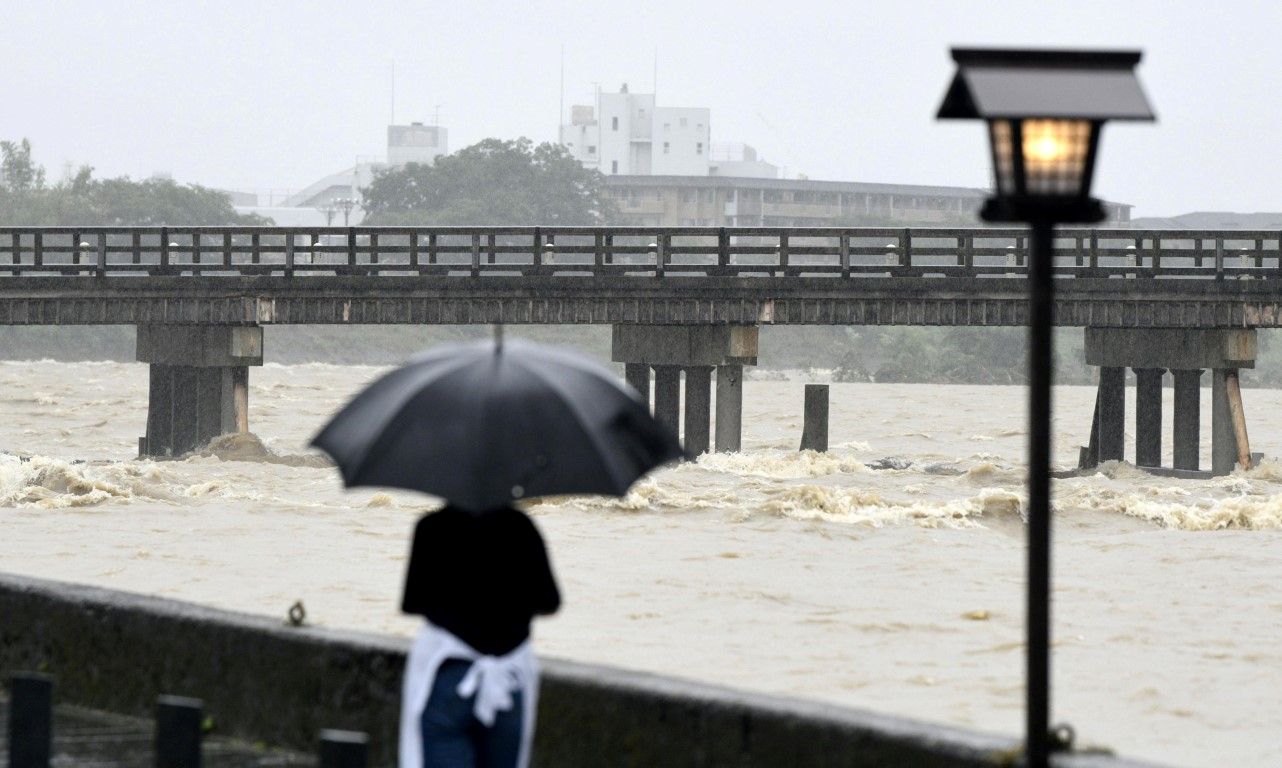 A resident watches Togetsu Bridge and the swollen Katsura River after heavy rain in Kyoto,...