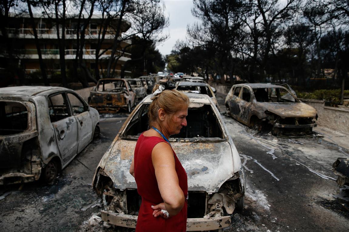 A woman surveys damage next to cars burnt out by the fire at the village of Mati, near Athens....