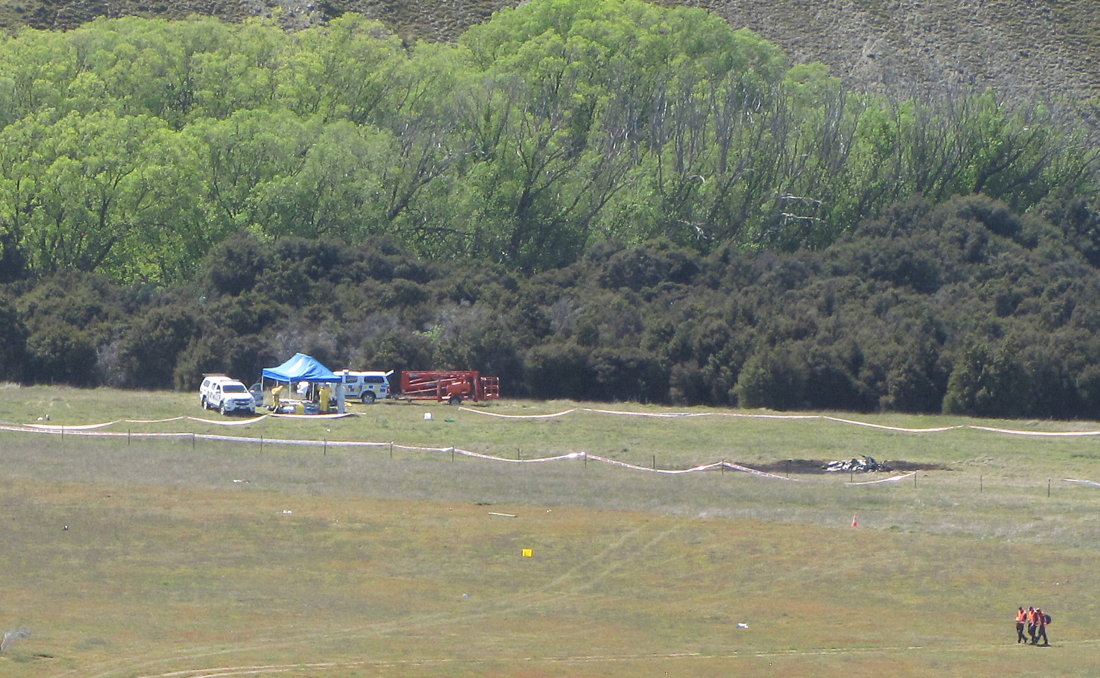 Investigators search the area around the wreckage of the Hughes 500 which lies under the blue canopy near the river. Photo: Mark Price