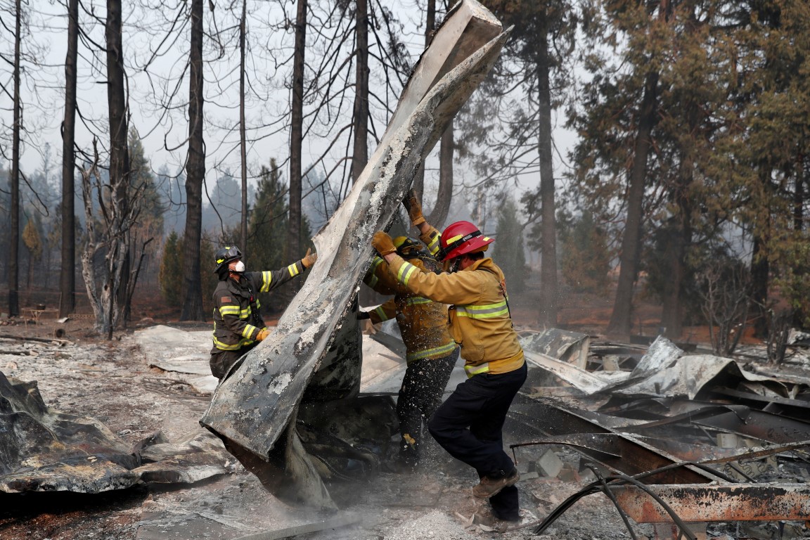 Firefighters move debris while recovering human remains from a trailer home destroyed by the Camp...