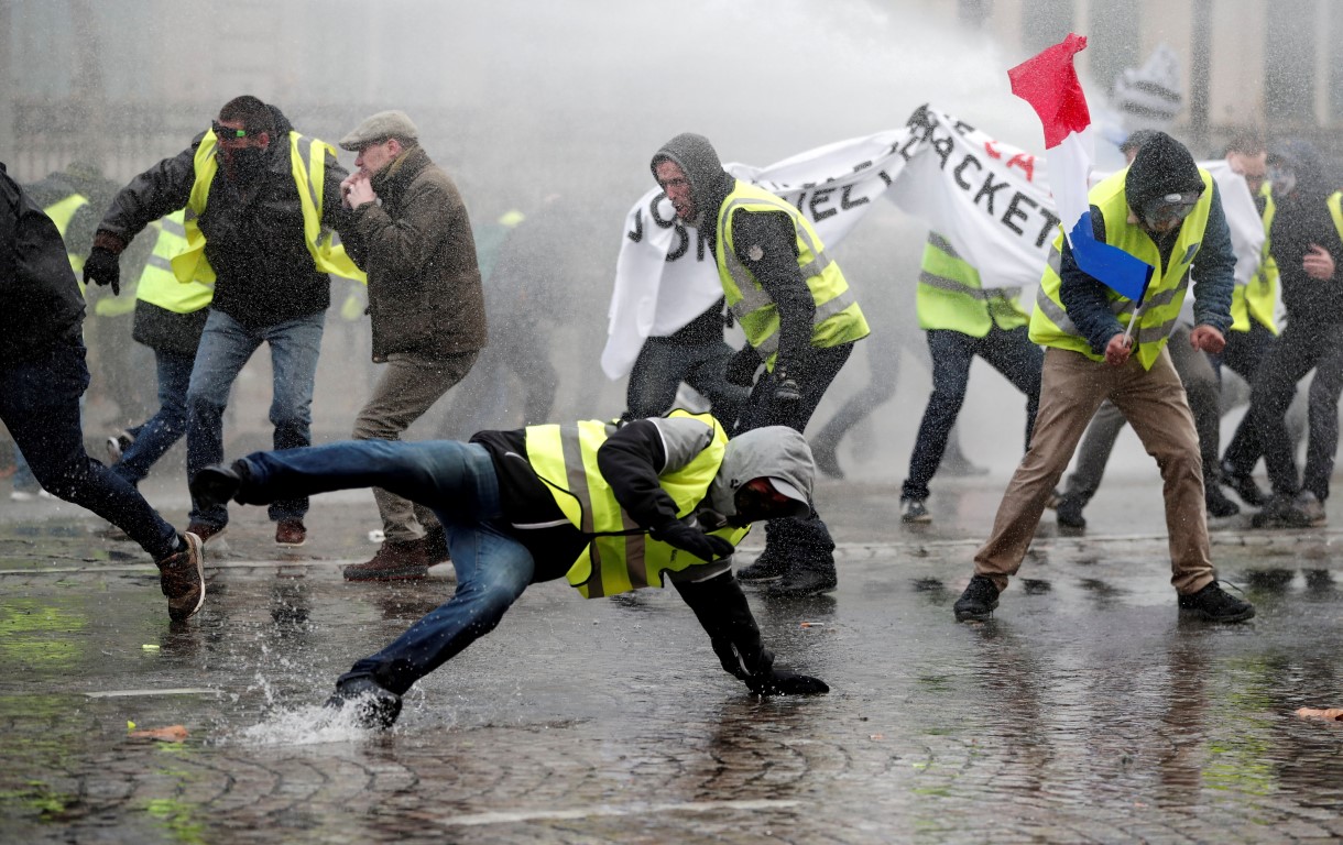 Protesters face a water canon fired by police during recent clashes on the Champs-Elysees in...