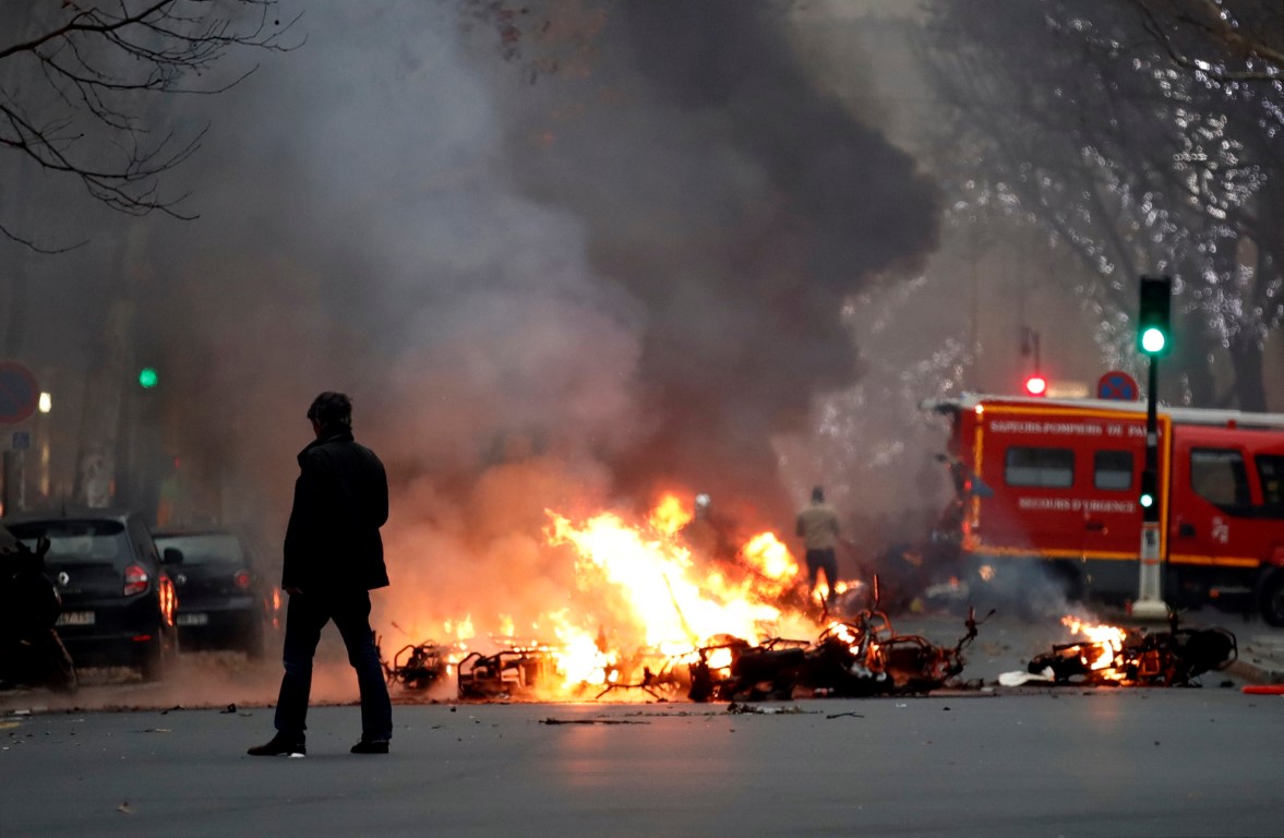 A man stands near a fire during a demonstration by the "yellow vests" movement at Boulevard Saint...