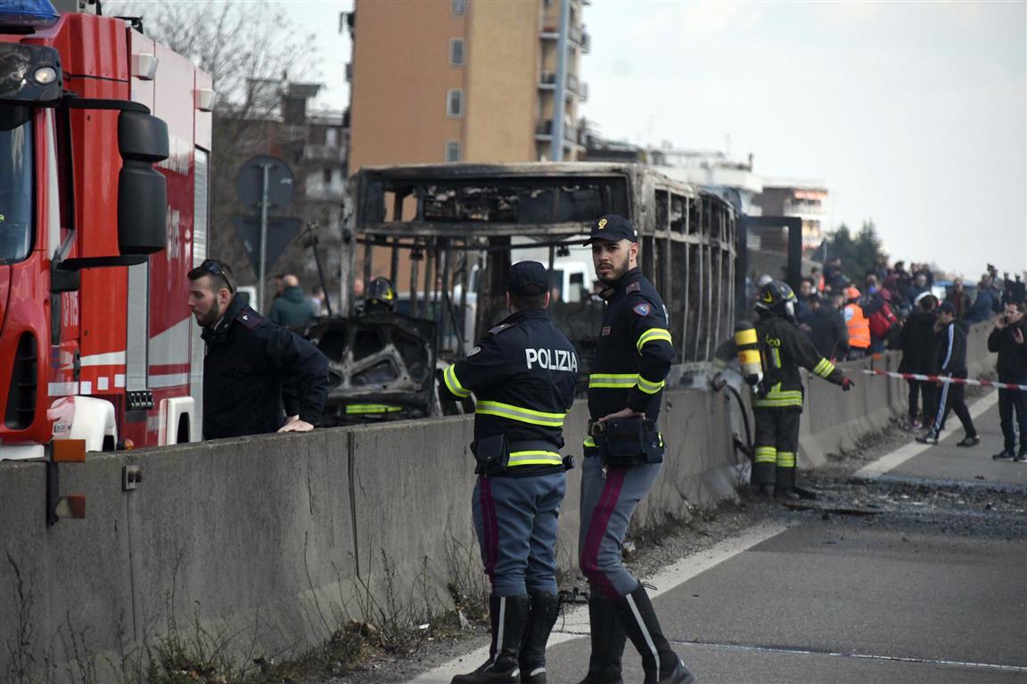 Firefighters and police officers stand by the gutted remains of the bus in San Donato Milanese,...