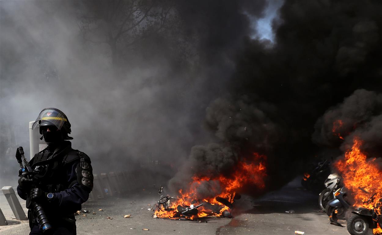 A police officer stands next to the burning motorcycles during a demonstration on Act XXIII (the...