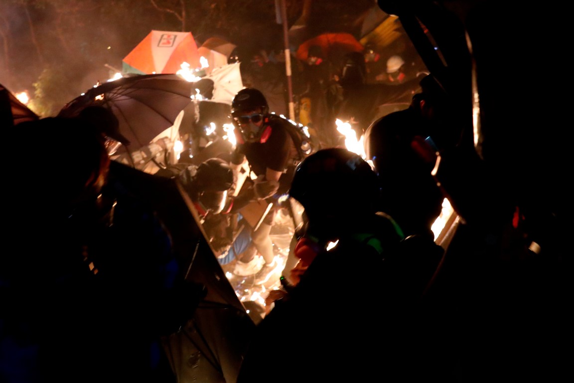 Anti-government protesters take cover during a standoff with riot police at the Chinese...