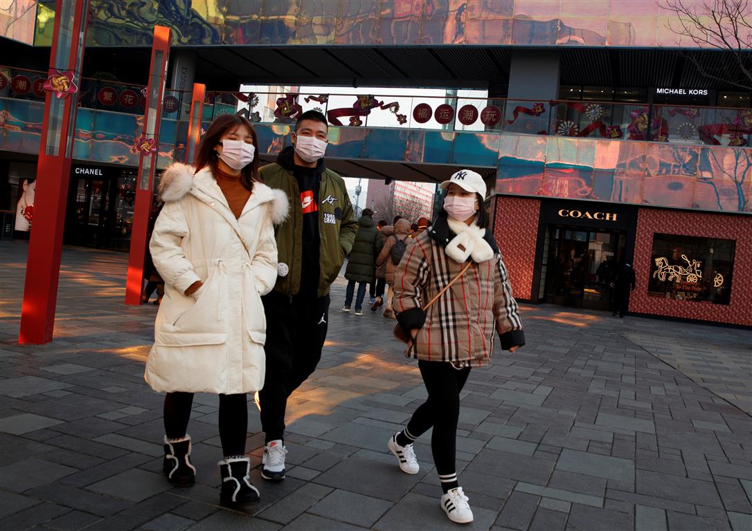People wearing face masks walk past luxury boutiques in the Sanlitun shopping district in Beijing...
