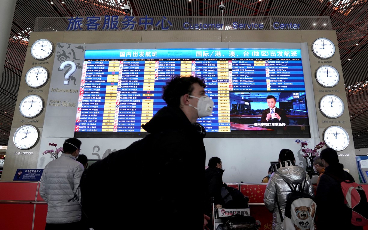 A traveller wearing a mask walks past a departures information board at Beijing International...