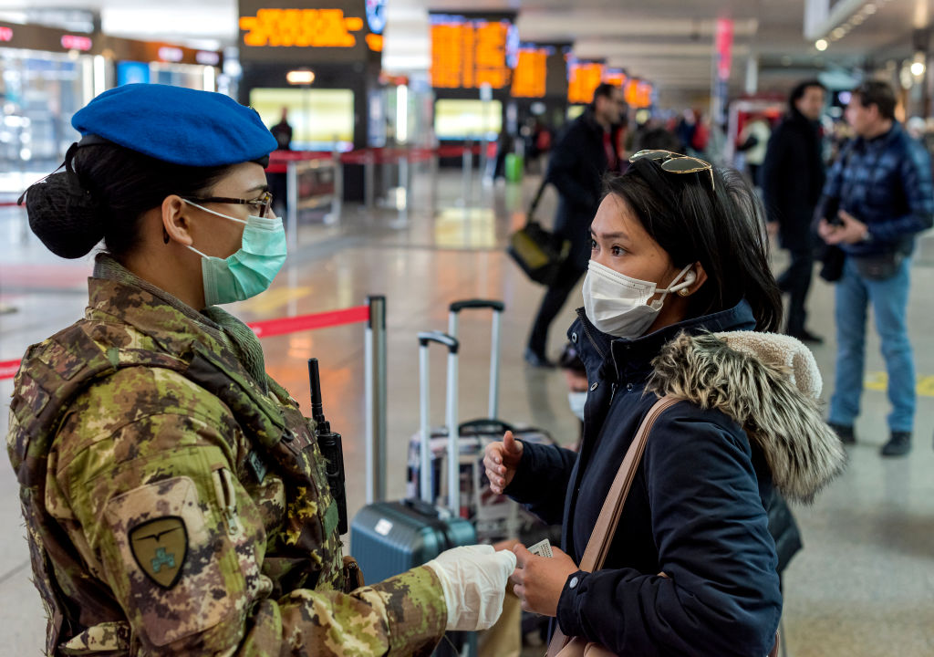 A soldier wearing a protective face mask talks with a woman wearing a respiratory mask as part of...