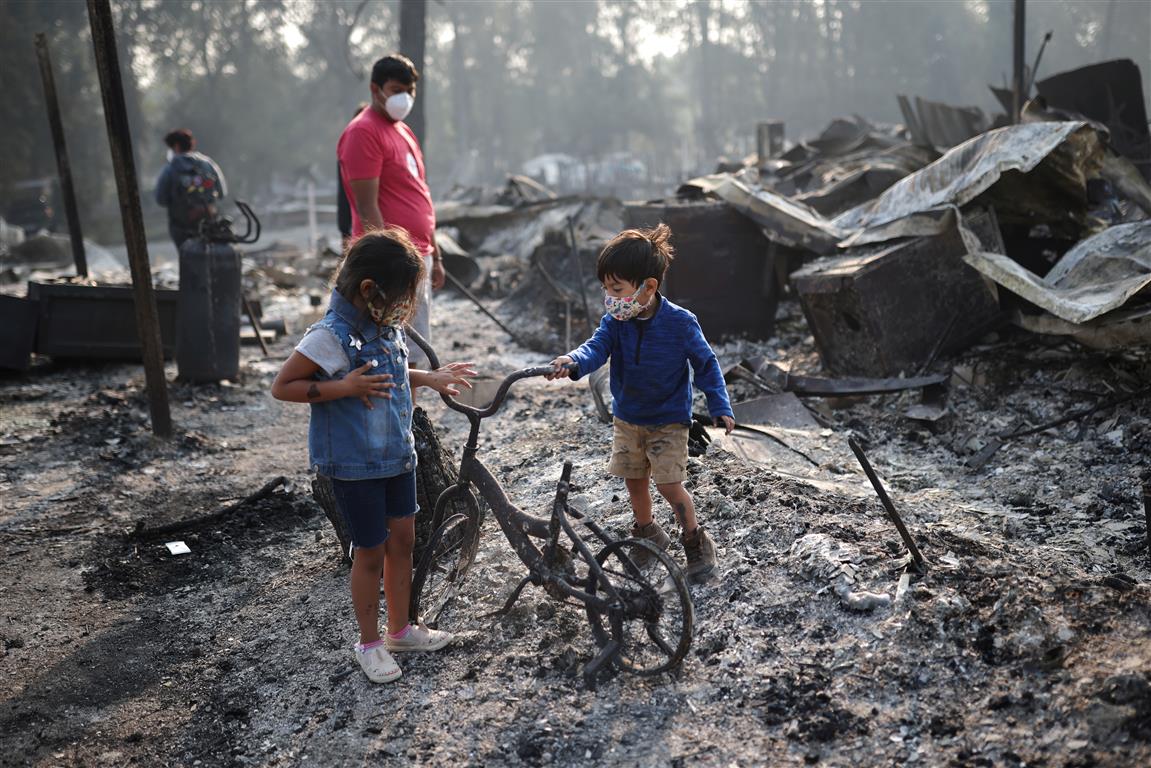 Children look at a burned bicycle after wildfires destroyed a neighbourhood in Bear Creek,...