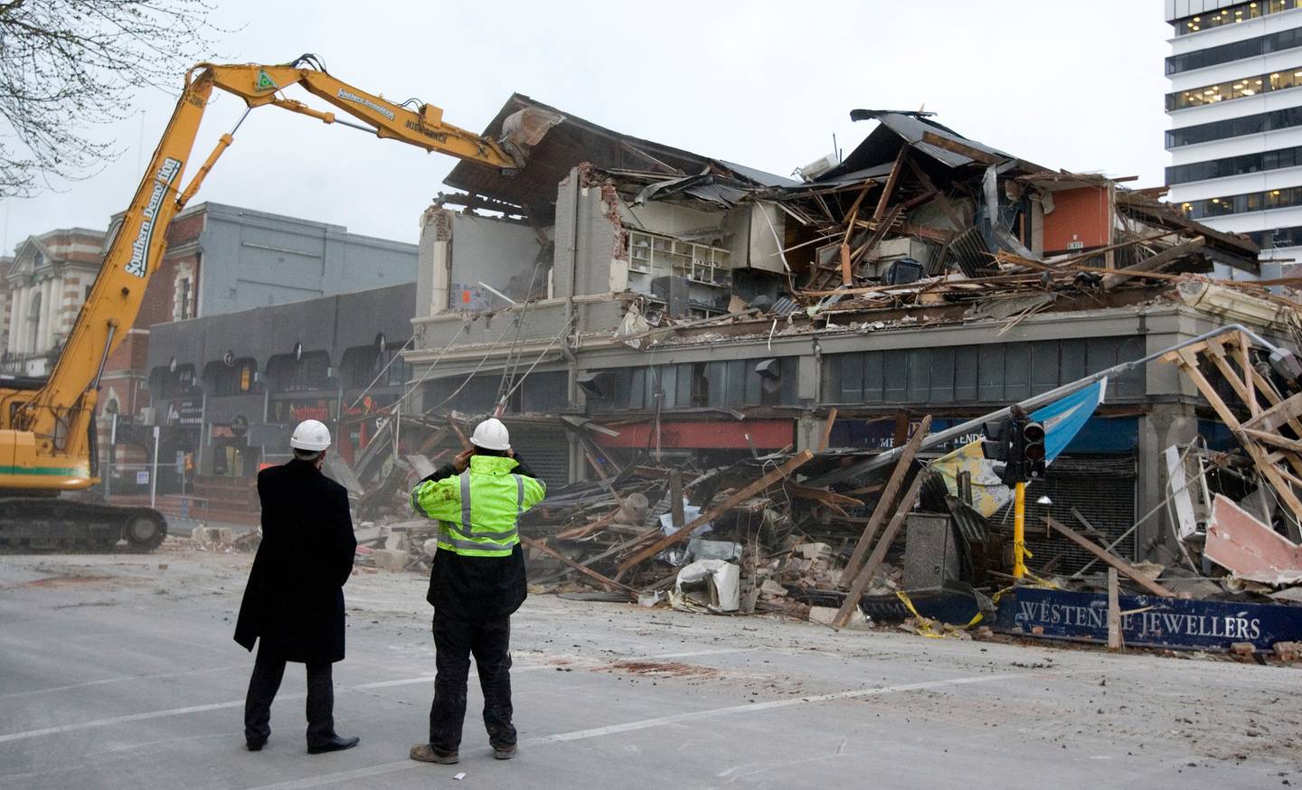 Insurance and demolition workers watch as the earthquake-damaged building on the corner of...