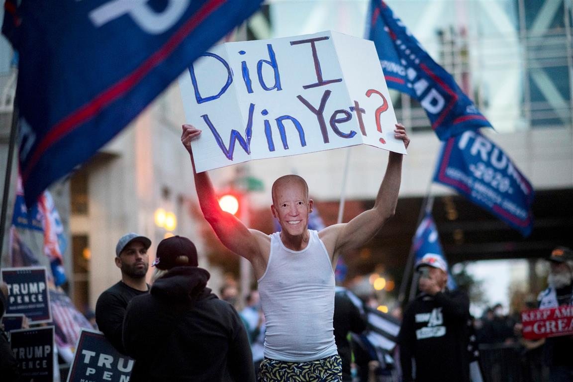 A Trump supporter carries a sign while wearing a Joe Biden mask during a protest outside of the...