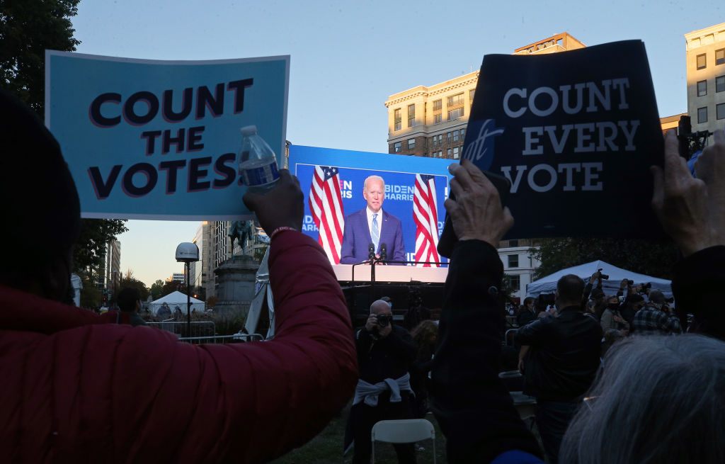 People hold up "Count the Votes" signs as presidential candidate Joe Biden appears on a large...