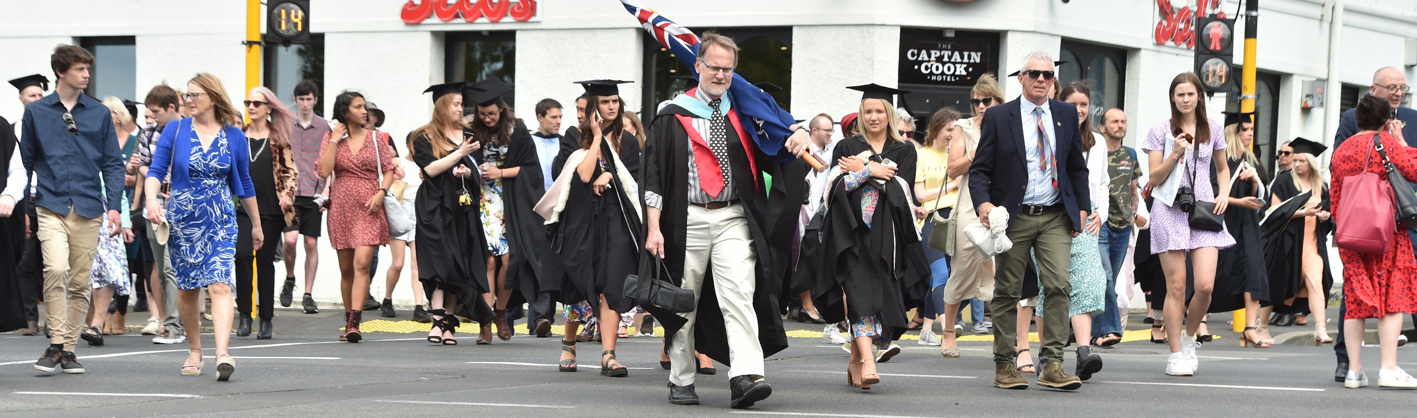 Caroline Freeman College warden Chris Addington, carrying a New Zealand flag, and students and...