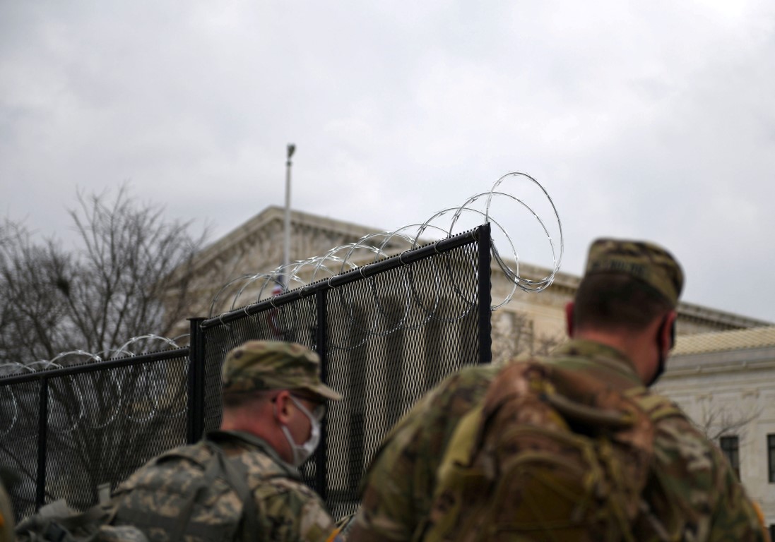 Officers from the National Guard walk near a fence lined with barbed wire at the Capitol grounds...