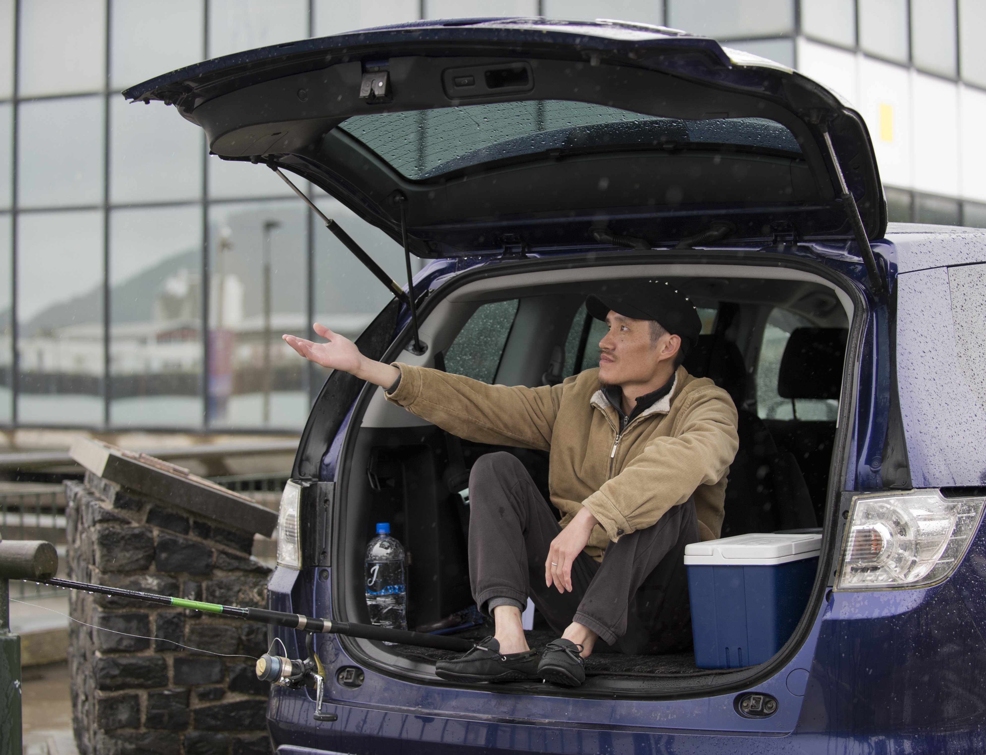 Yi Bai, of Dunedin, shelters from the rain in the back of his station wagon as he fishes for...