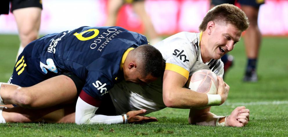 Jordie Barrett of the Hurricanes dives over to score a try while being tackled by Highlander...