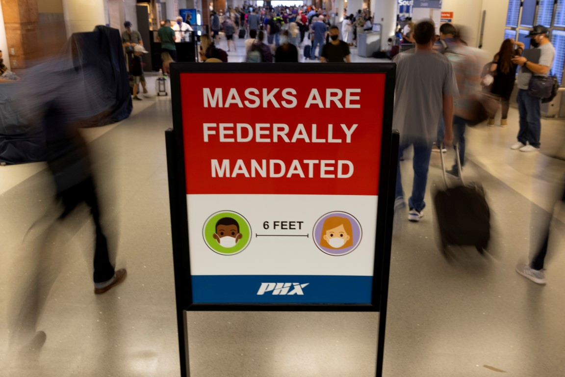 Travellers make their way past a sign mandating face masks at Phoenix International Airport in...