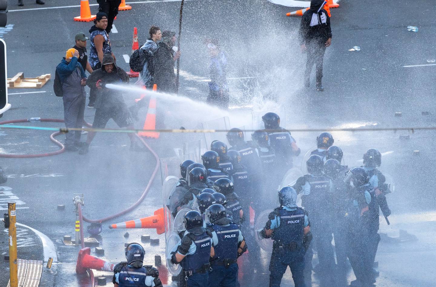 Police officers have a fire hose turned on them by protesters on Bowen Street on day 23 of the...