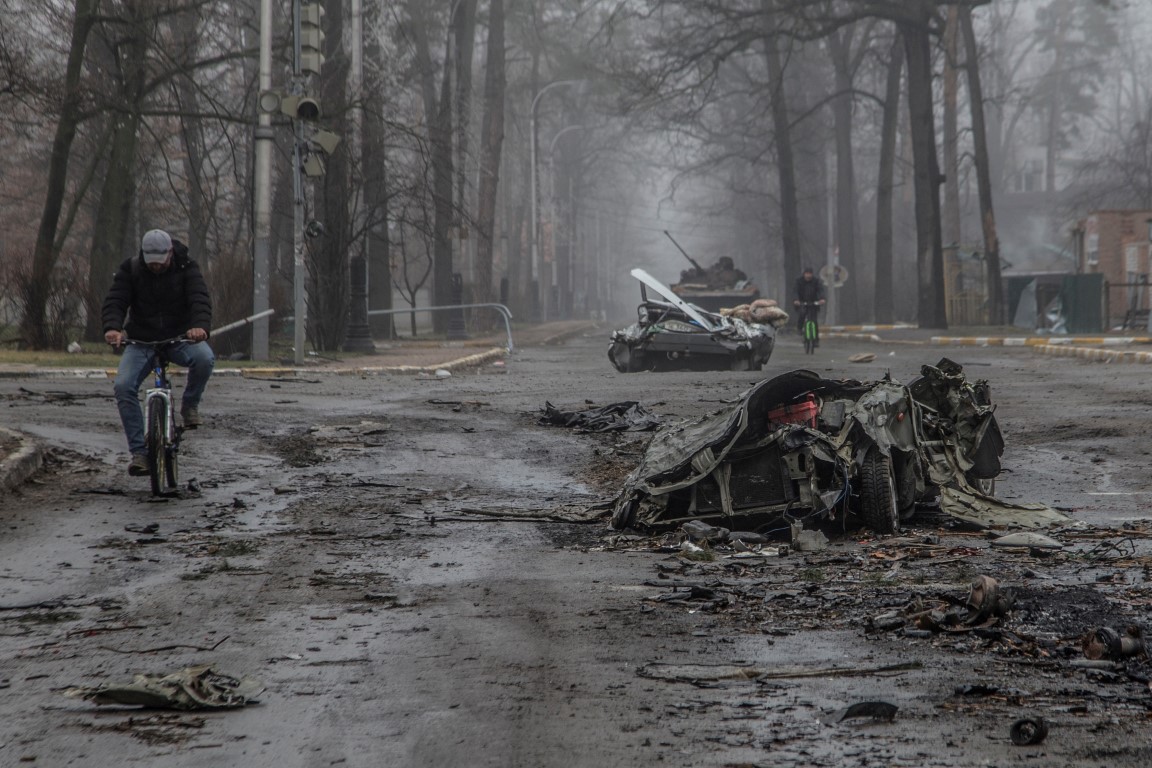 Residents ride bicycles past flattened cars on a street in the town of Bucha, in Kyiv region....