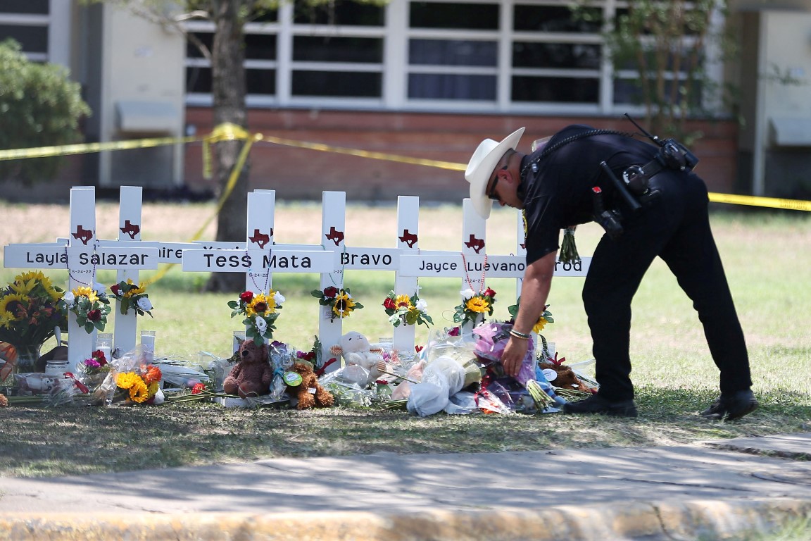 A police officer places flowers at a memorial to victims of the shooting at Robb Elementary...