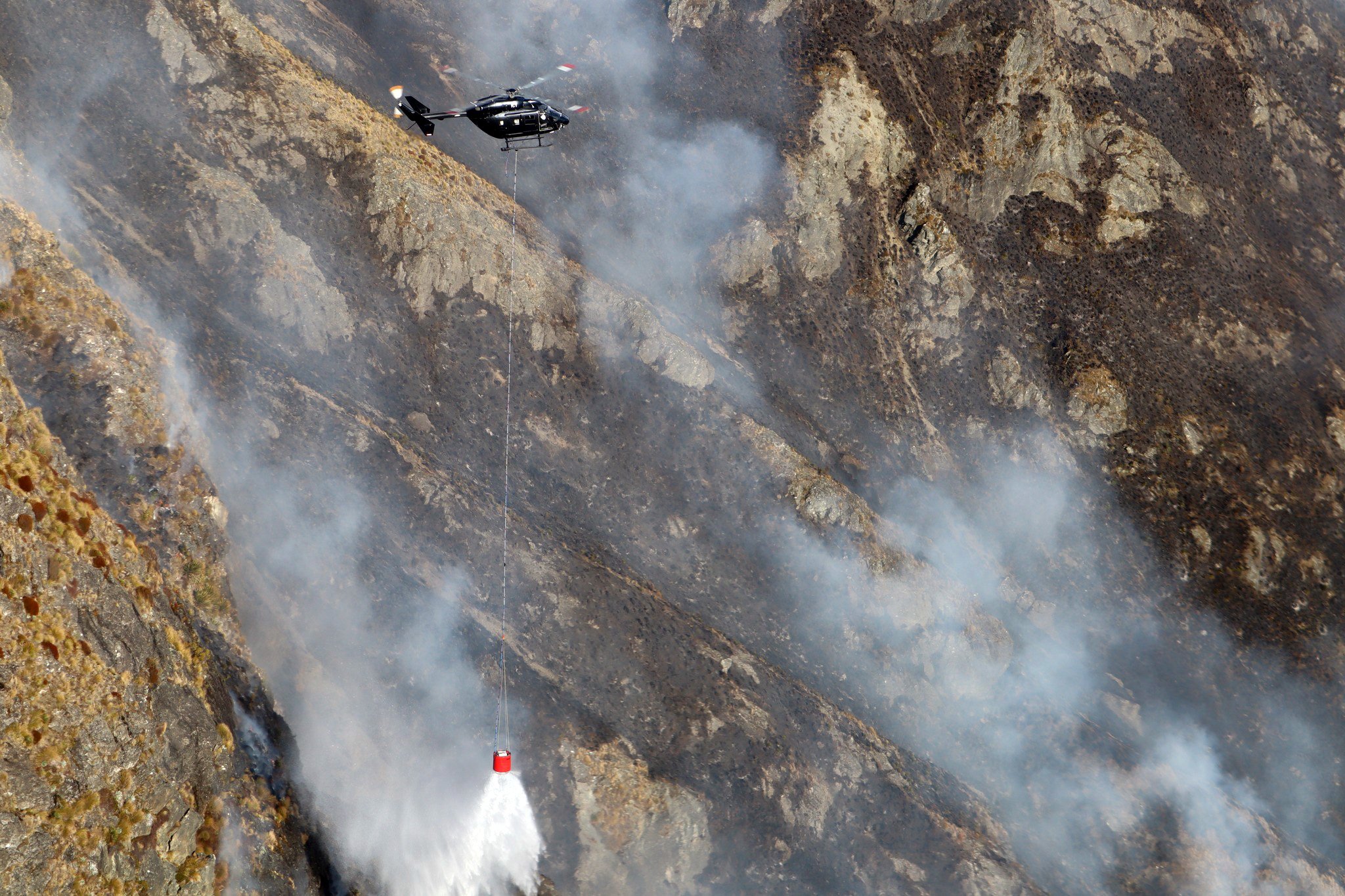 One of six helicopters working to contain the fire burning in steep terrain on Mt Creighton.