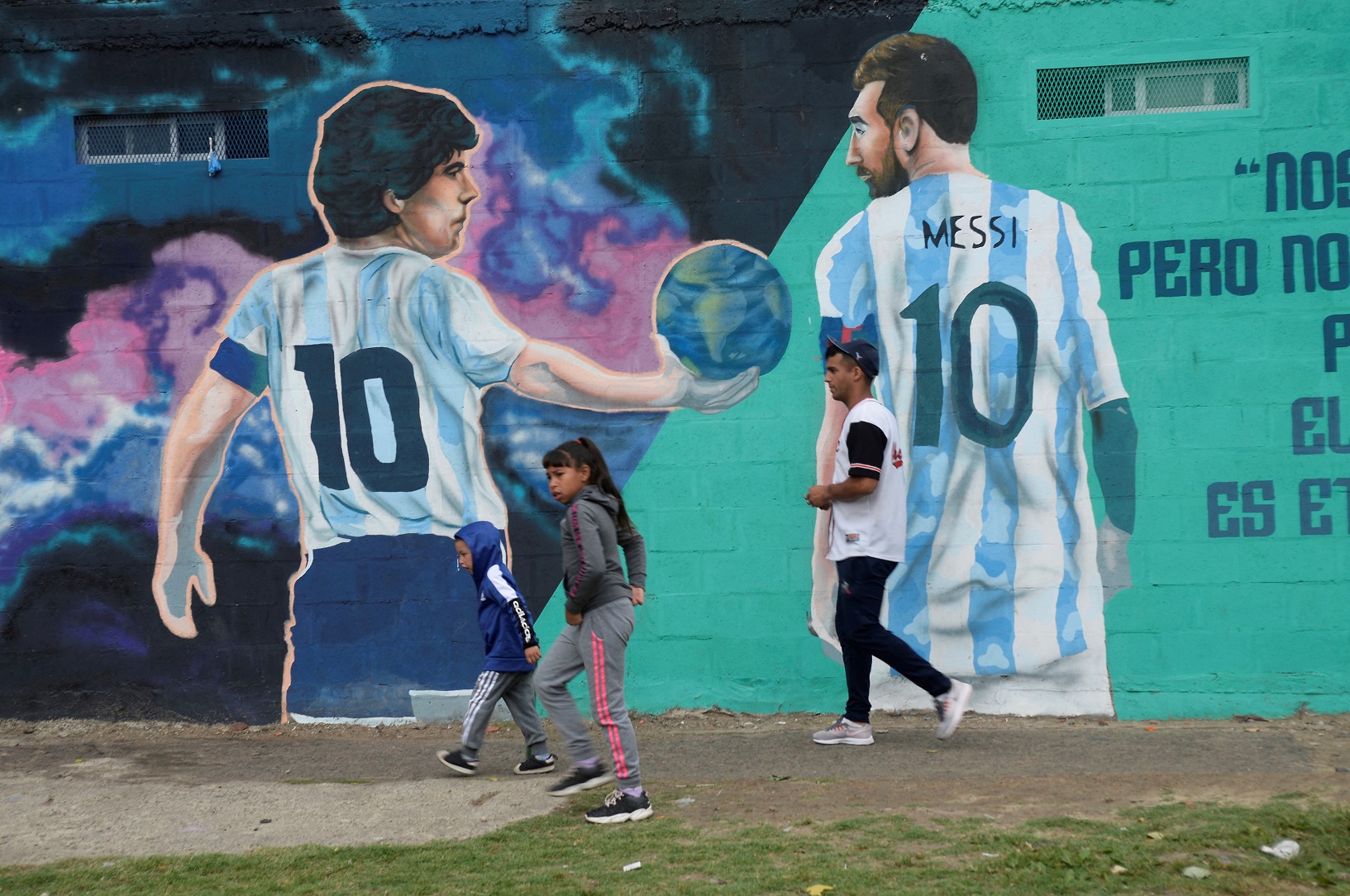 Pedestrians walk past a mural depicting late soccer legend Diego Armando Maradona and PSG's...