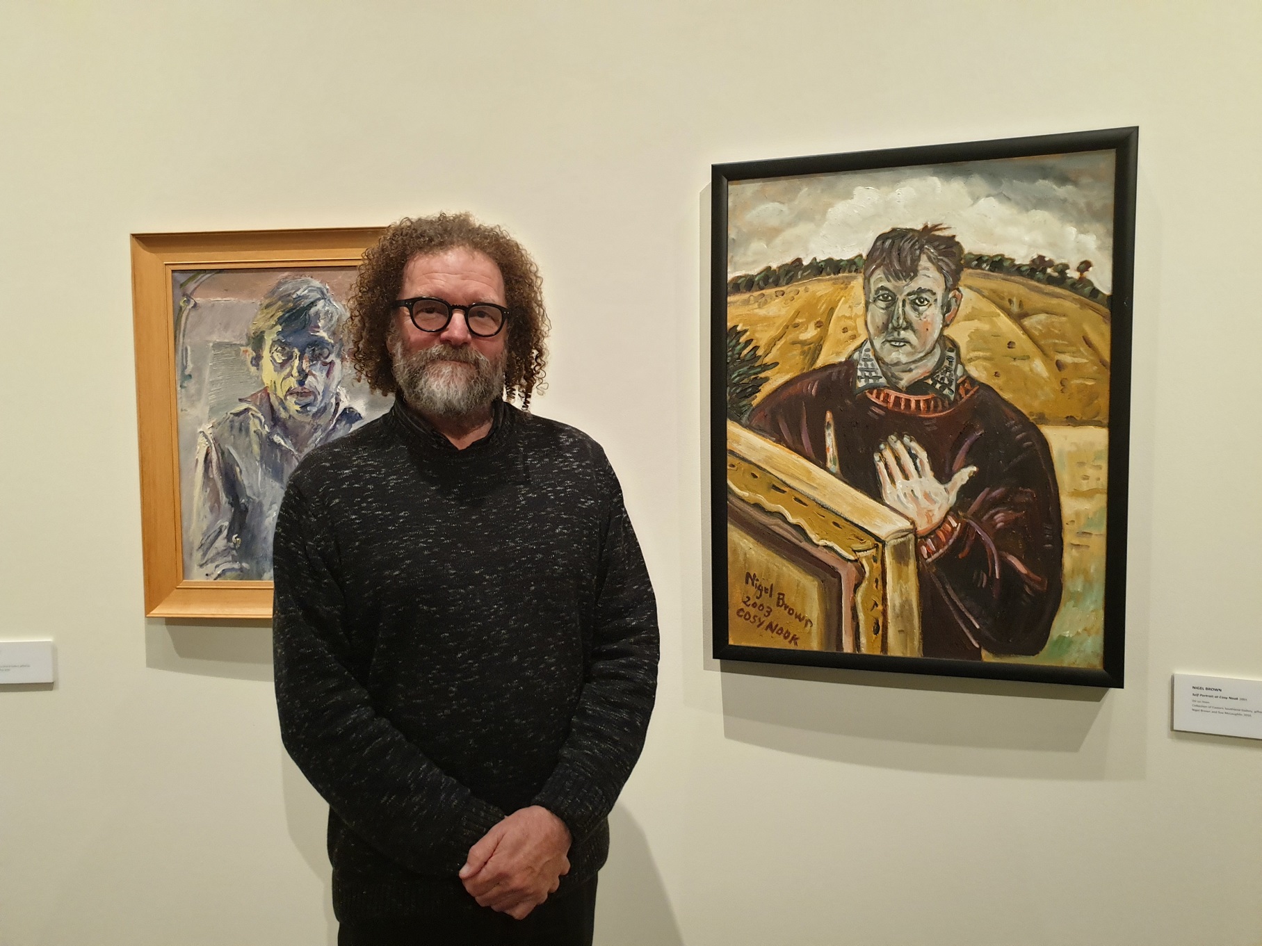 "Persona" curator Jim Geddes in the gallery of portraits. To his left is an Alan Pearson portrait...