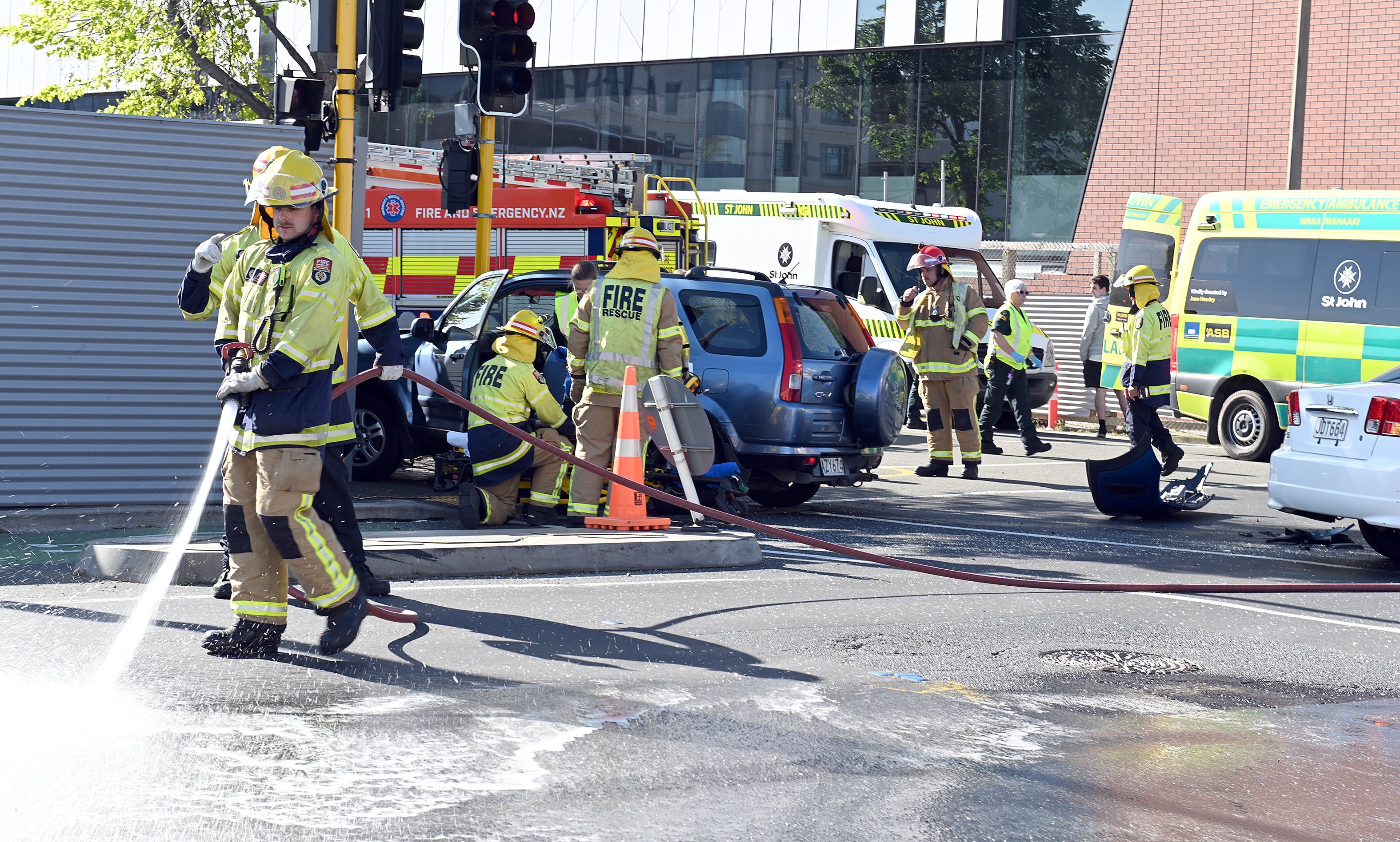 A firefighter washes debris from the road as a person is extricated from a car after the crash at...