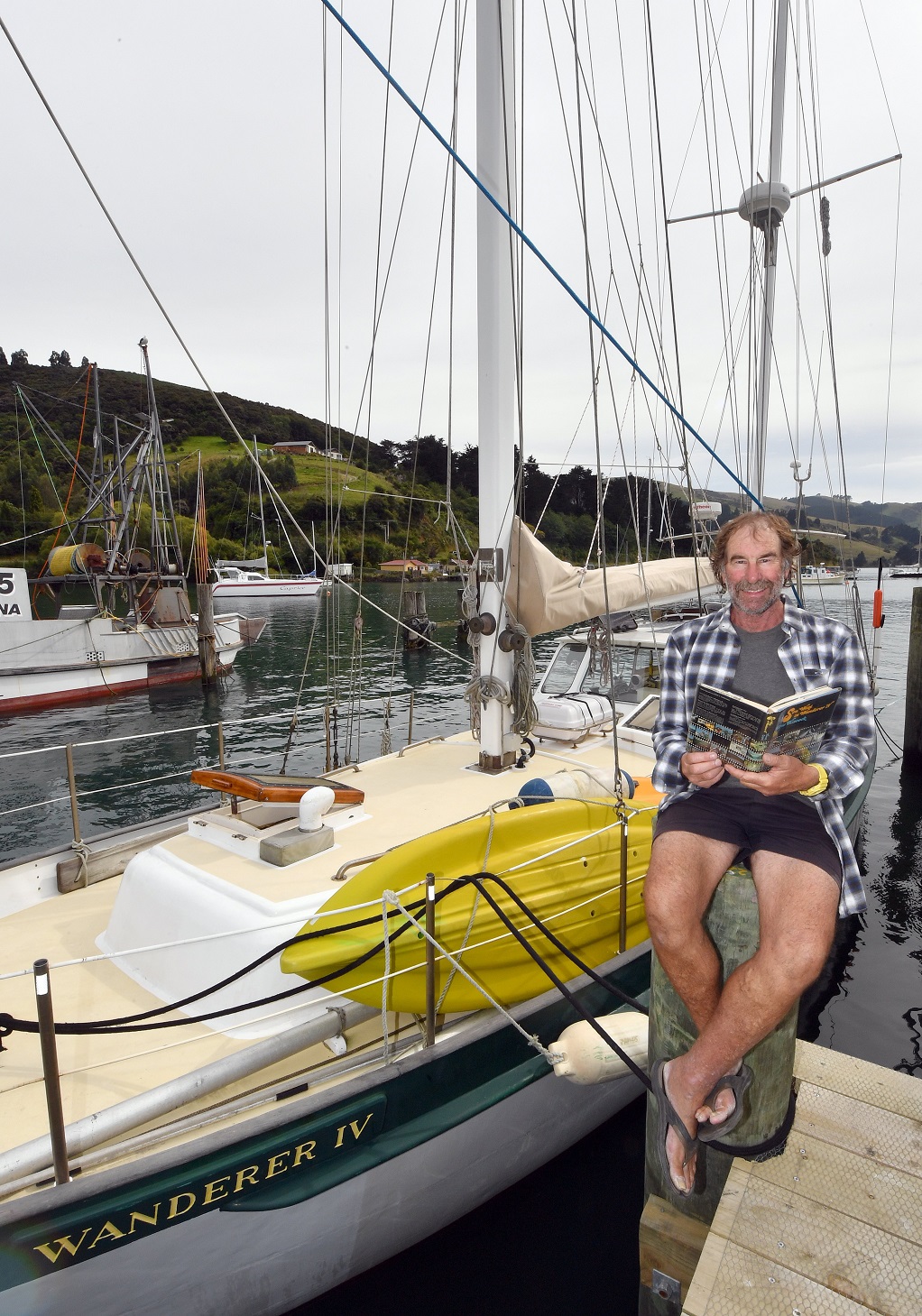 Trevor Whelan sits beside his yacht Wanderer IV as he reads a cruising book, Sou’West in...