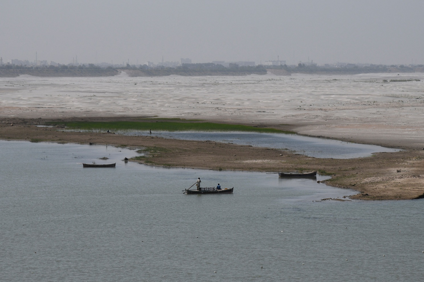 A man navigates a boat in the water next to the dry riverbed of the Indus River in Hyderabad,...