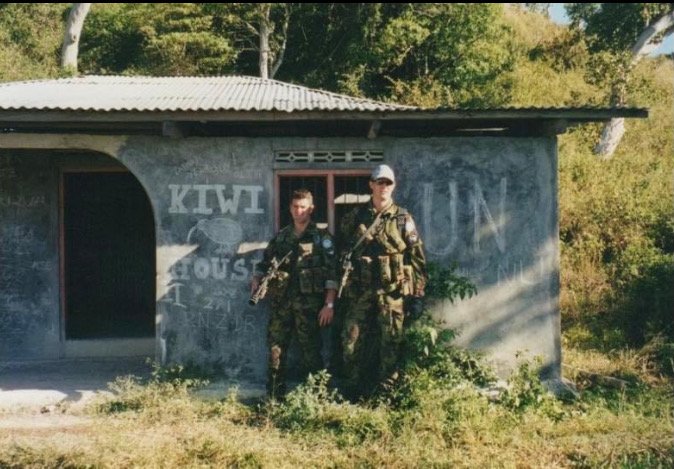 Two unknown soldiers stand in front of the carved graffiti left by Aaron Horrell in East Timor in...