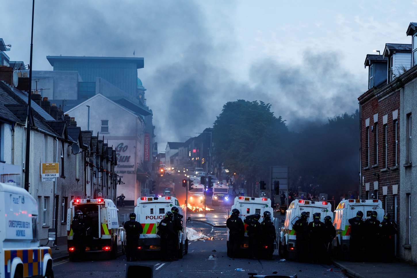 Officers stand guard behind police vehicles during clashes on the second night of riots in...