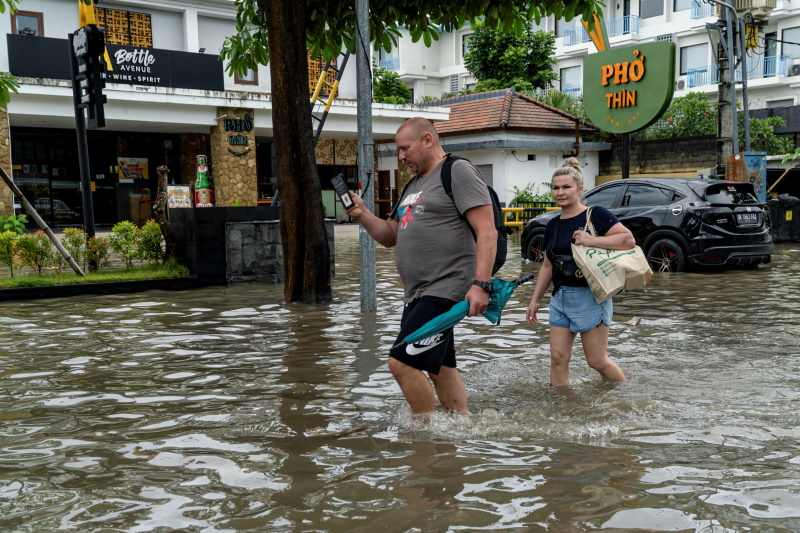 Tourists wade through a flooded road yesterday following overnight heavy rains in Legian, Badung,...