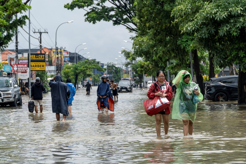 People carrying their belongings wade through a flooded street following overnight heavy rains in...