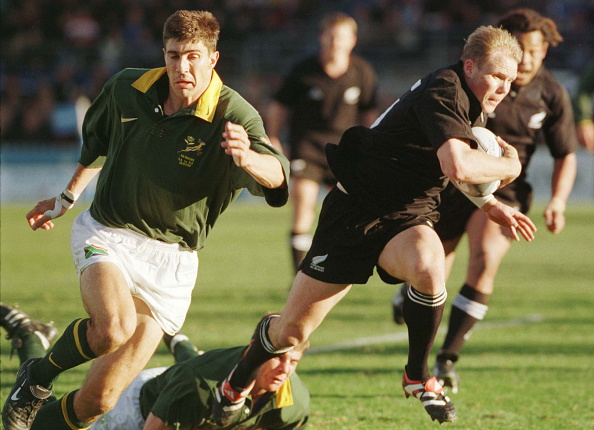 Jeff Wilson runs with the ball for the All Blacks as Springboks winger Pieter Rossouw chases him...