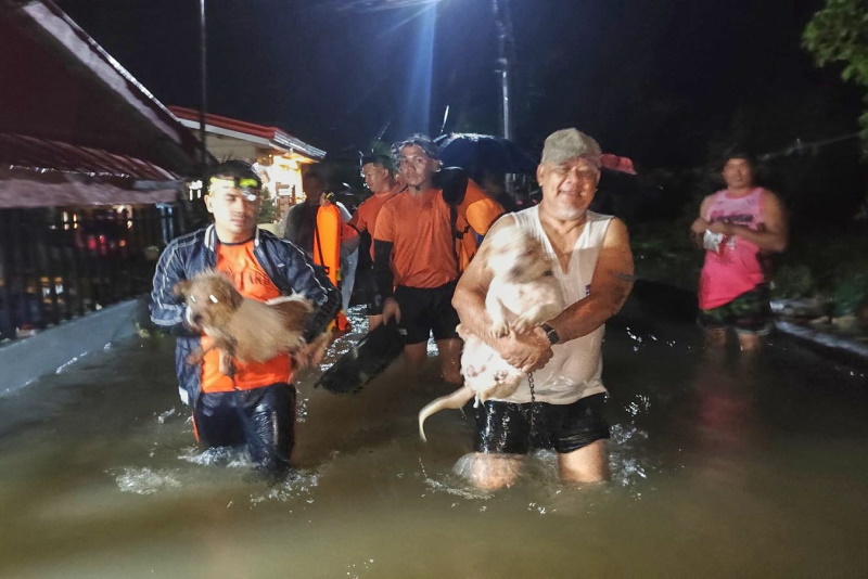 Residents and their dogs are evacuated by rescuers as floods rise due to Typhoon Bualoi in Ormoc,...