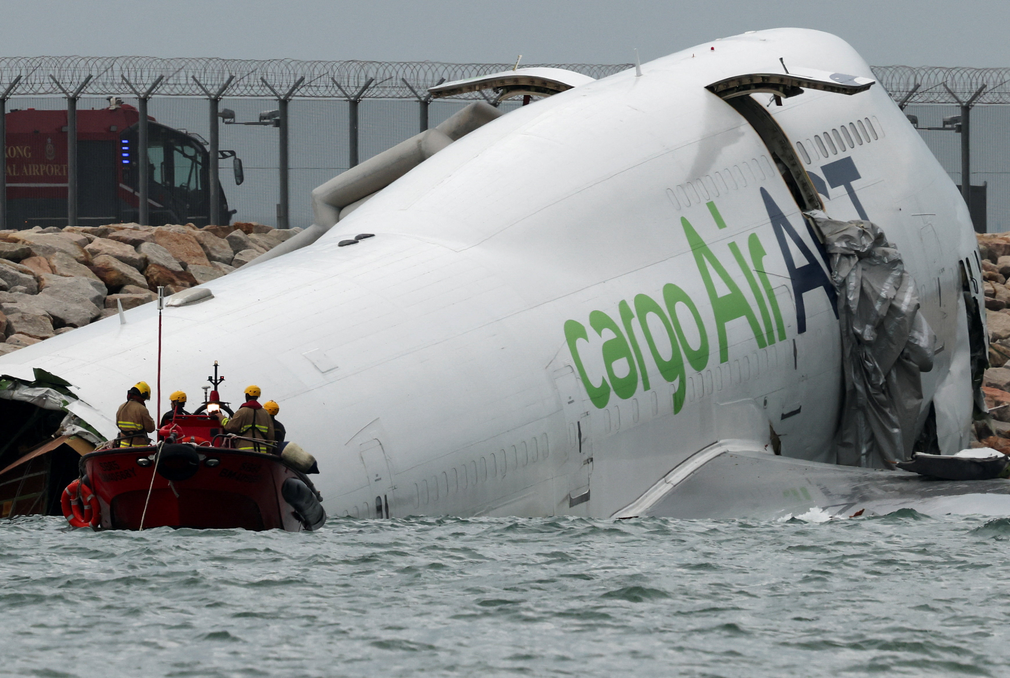 Emergency workers near the cargo plane lying partially in the sea after it veered off the runway...
