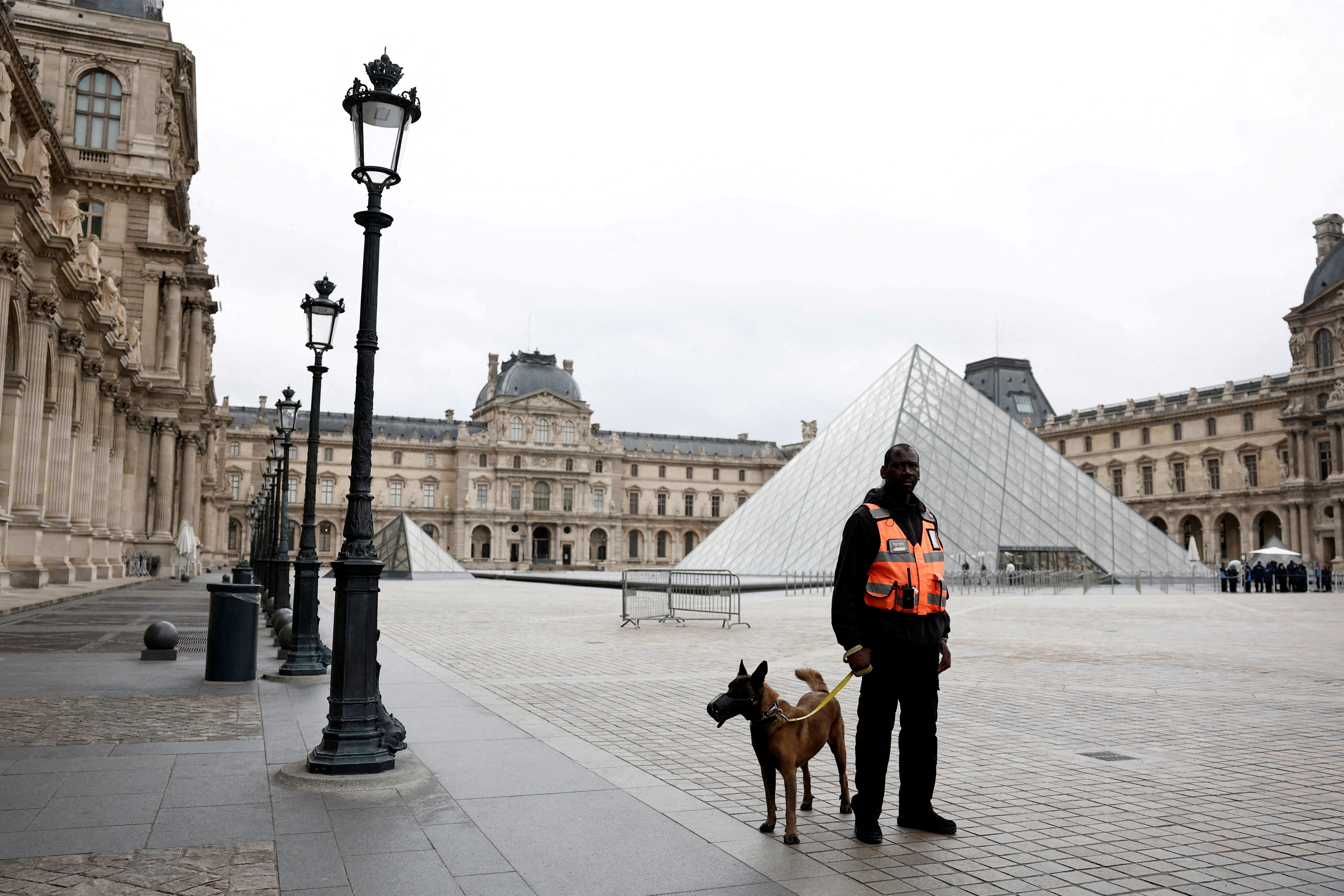 A security employee with a dog stands near the glass Pyramid of the Louvre Museum as the museum...