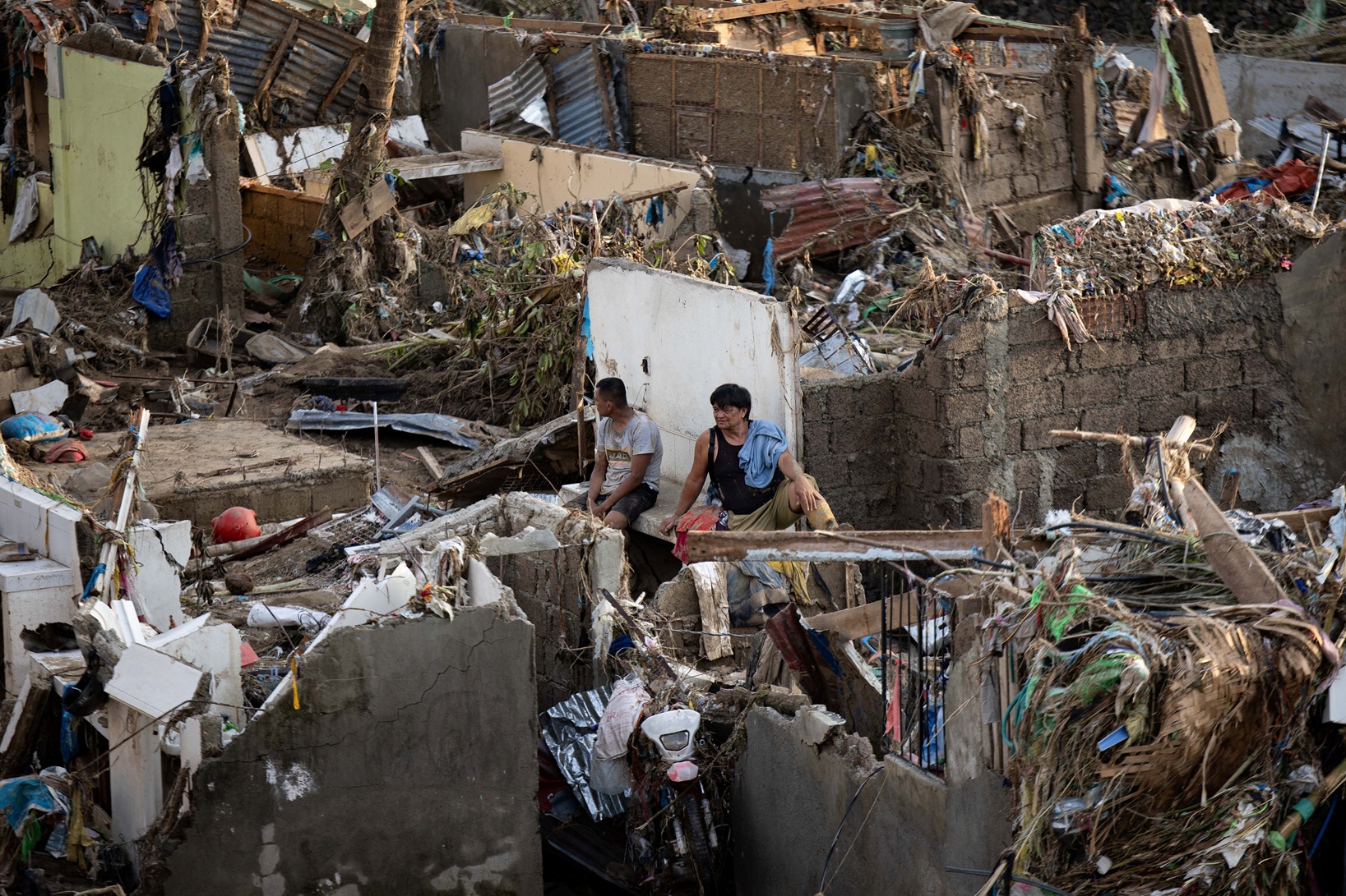 Men sit amid the remains of houses destroyed in floods brought on by Typhoon Kalmaegi in Talisay...