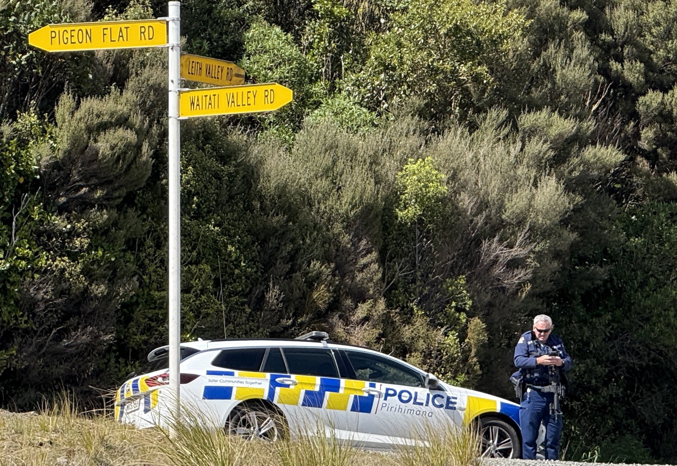An armed police officer stands at a cordon at the intersection of Dunedin-Waitati Highway (State...