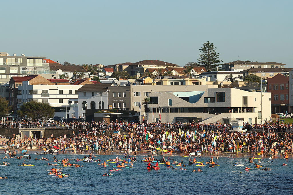 People gather at Bondi Beach as surfers take part in a paddle out to honour the victims and those...