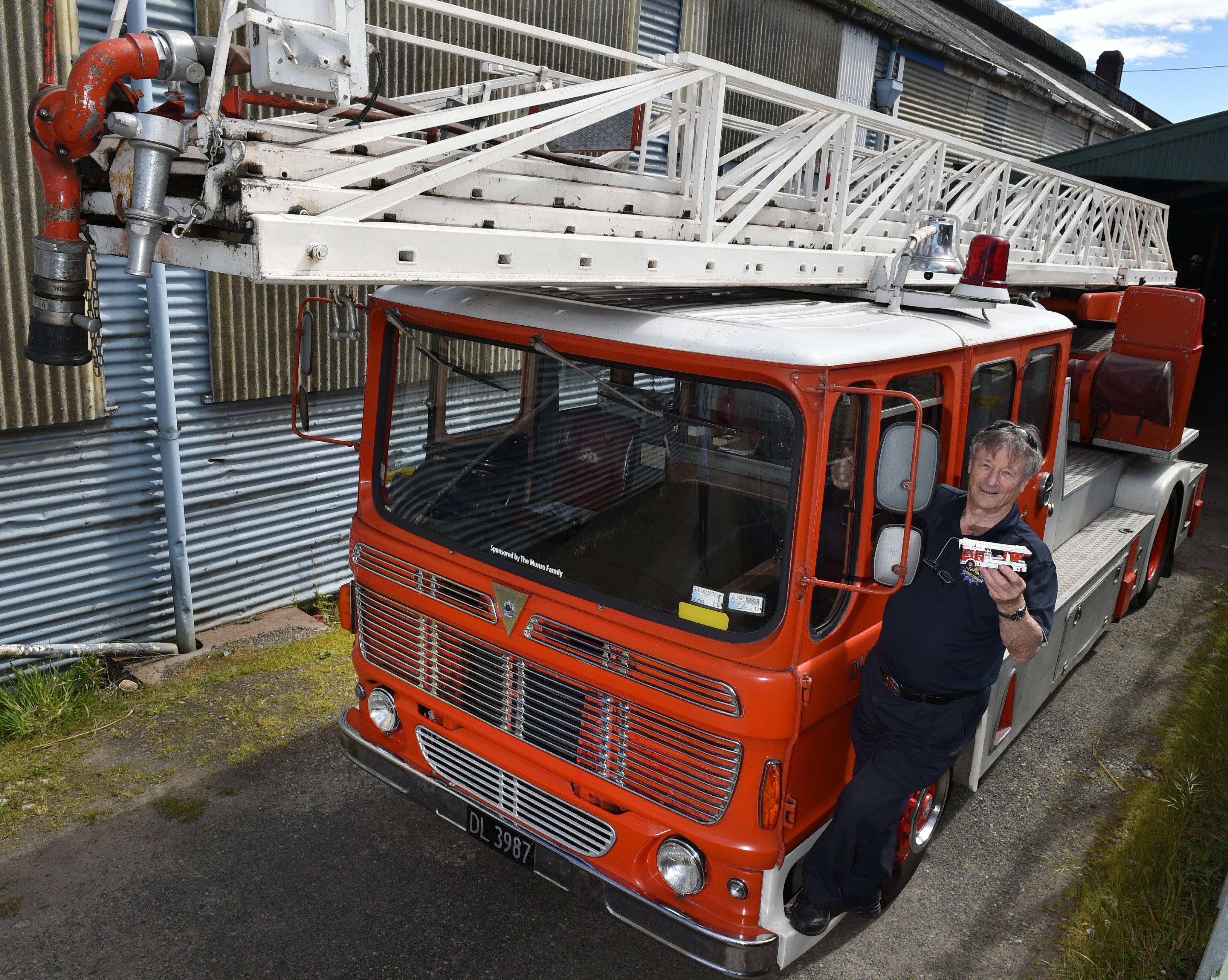 Retired firefighter Errol Thompson stands on the Merryweather ladder truck, holding a model of...