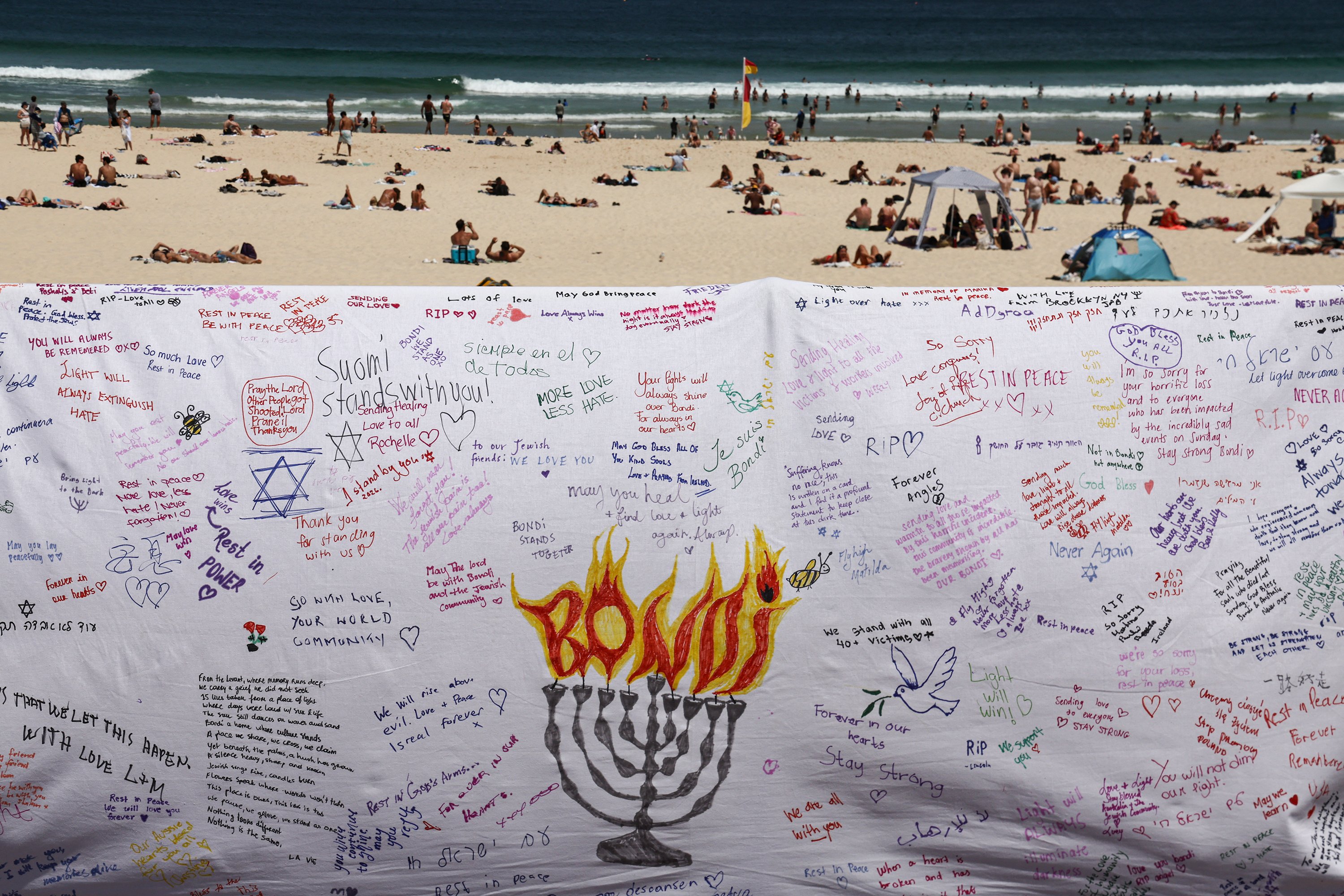 Beachgoers return to Bondi, photographed from behind a piece of cloth bearing messages left by...