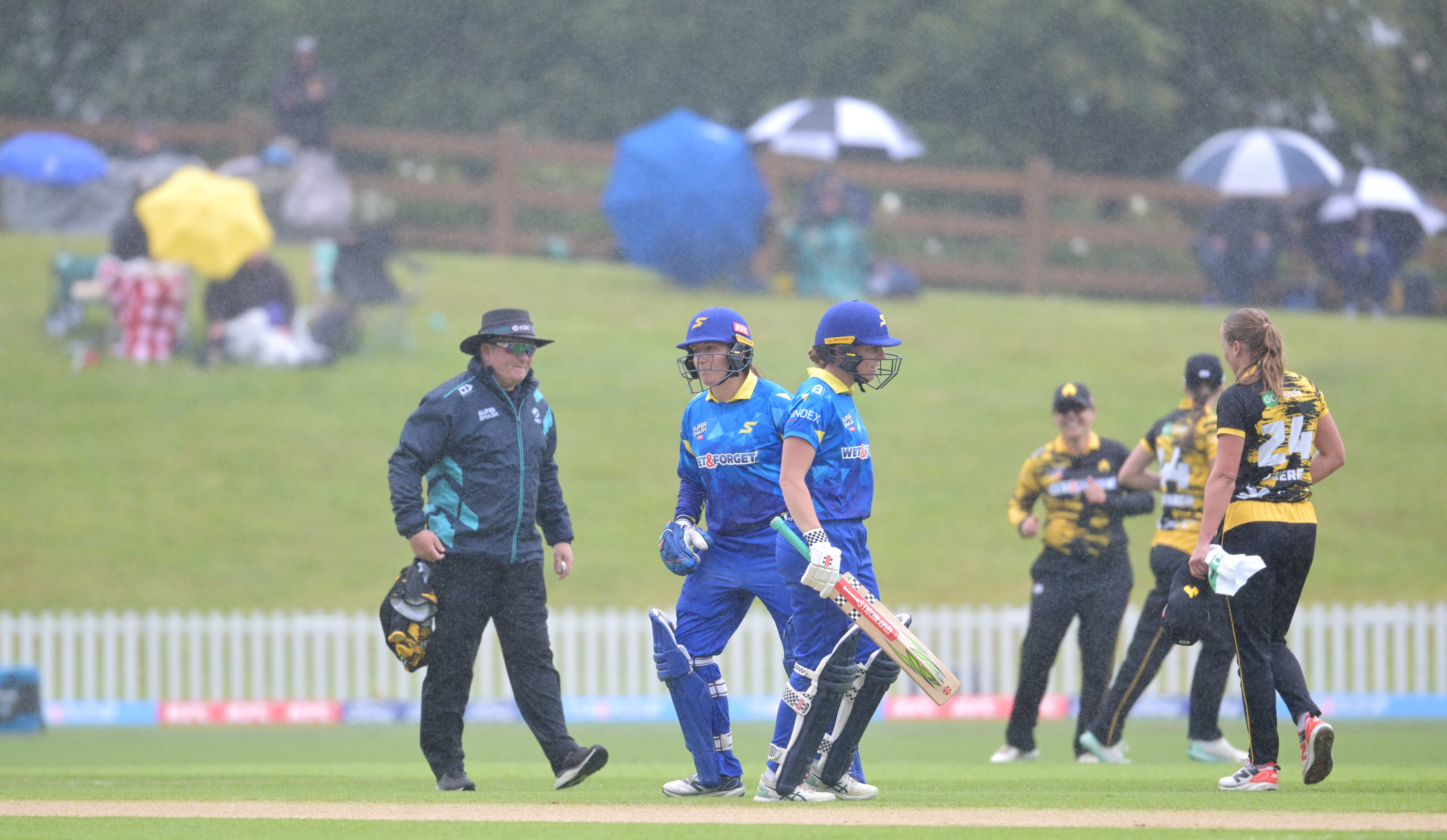 Cricket fans hover under umbrellas during the rain at the University Oval yesterday. The Sparks...