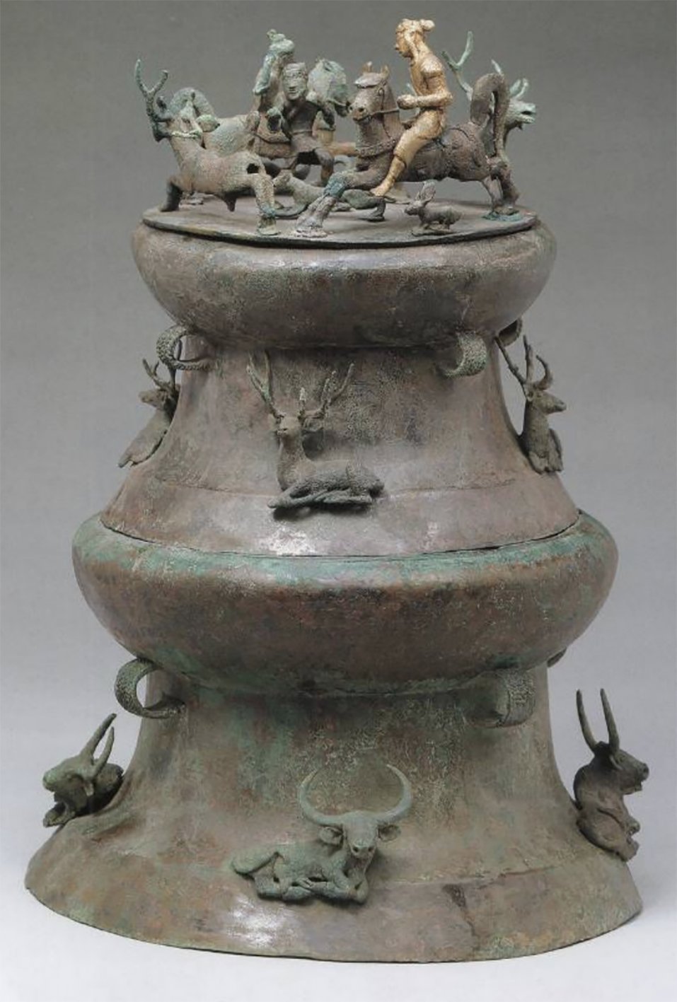 A bronze vessel filled with cowrie shells ornamented with a golden horseman hunting deer. Source:...